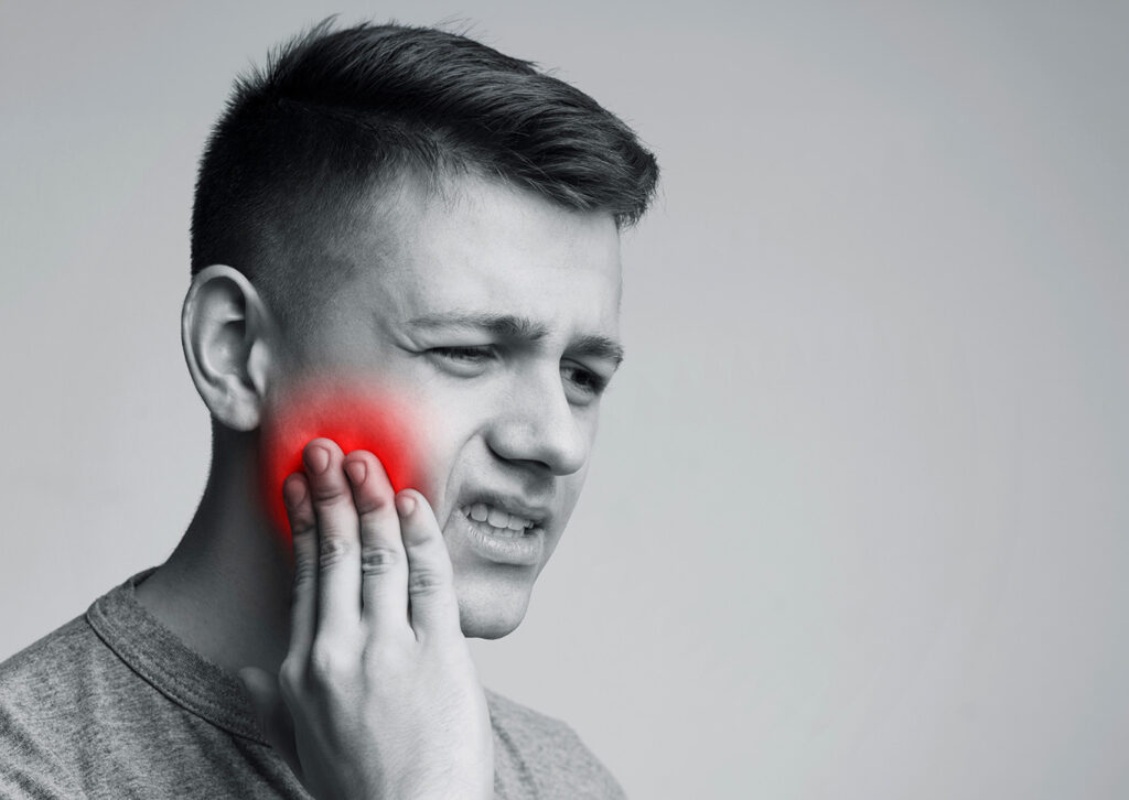 A man holds his cheek with a pained expression; a red highlight on his cheek indicates pain or toothache.