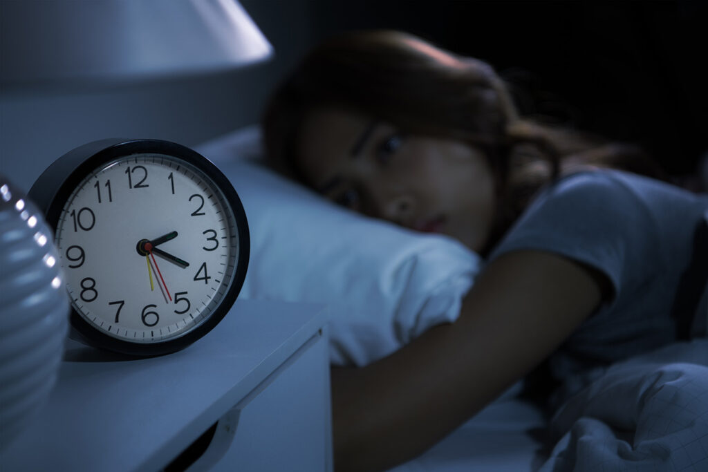 A woman lies awake in bed at night, looking at a clock on a bedside table showing the time as 2:15.