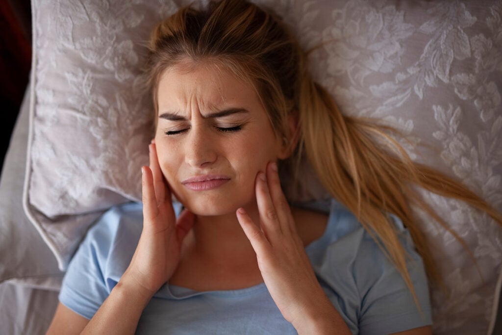 Bruxism teeth grinding symptoms shown by a woman touching her cheeks in discomfort
