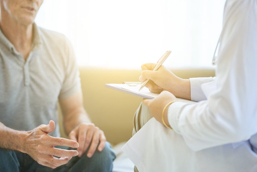 A doctor takes notes on a clipboard while talking with a patient who is gesturing with his hands. sleep disorder consultation.